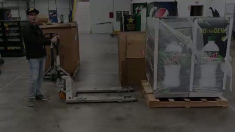worker moving a palletized load with a manual pallet jack in a beverage warehouse, face visible