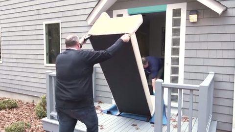two movers standing a wrapped sofa upright at the front door
