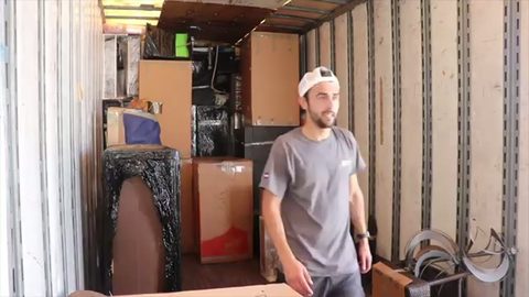 mover standing in a wall-to-wall packed long-distance moving trailer, face visible