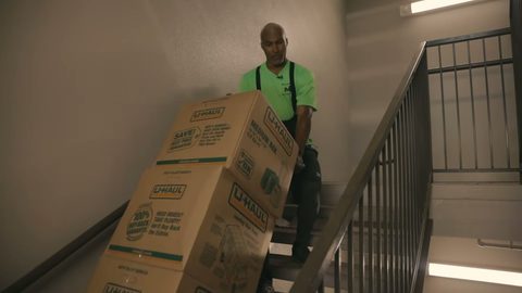 mover carefully bringing two stacked moving boxes down a stairwell on a hand truck, face visible