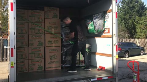 Mover securing the load inside the open rear of a box truck parked at the curb